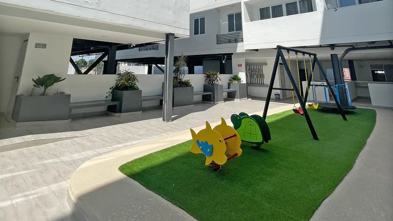 Área de juegos para niños con columpios y grama en el patio central de Acacias Versalles